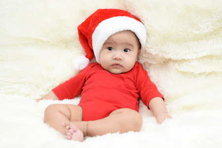 asian cute baby sitting on a soft cloth in the living room. Baby with Santa hat
