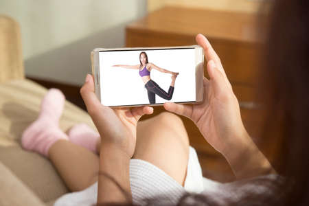 Beautiful woman playing phone on bed happily in morning. She watching the demonstration exercise through mobile phones. For women, health care and fitness It is important.の写真素材