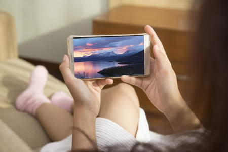 Beautiful woman playing phone on bed happily in morning. she was looking at the sights of Sweden on mobile phone.の写真素材