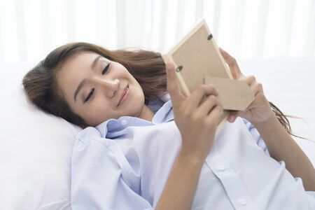Beautiful woman playing phone on bed happily in morning.の写真素材