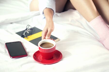 Beautiful woman drinking coffee on bed. Light colors vintage.の写真素材