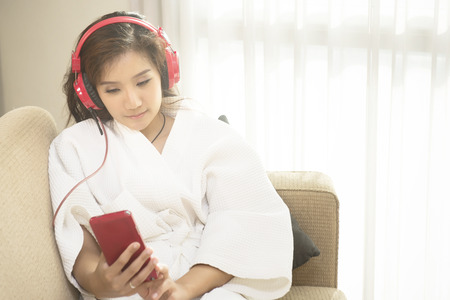 Beautiful woman playing phone in bedroom happily in morning.の写真素材
