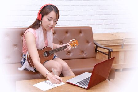 Women enjoy a drink, listen to music and play the ukulele in the living room.の写真素材