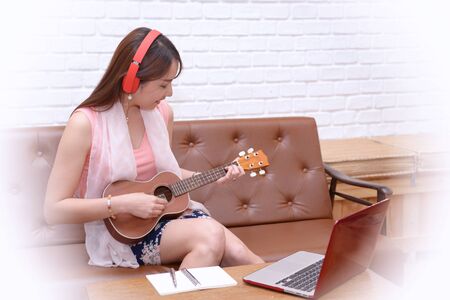 Women enjoy a drink, listen to music and play the ukulele in the living room.の写真素材