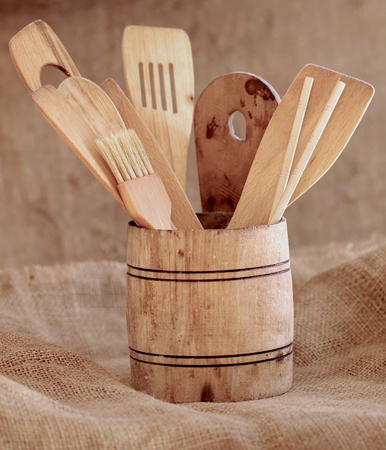 Vintage small wooden bucket with various kitchen utensils on a rustic background.の写真素材