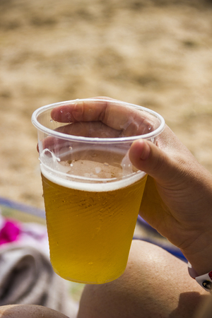 close-up plastic glass of beer in the hand at hot day on the beachの写真素材