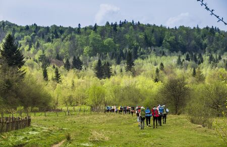 big group of hiking tourists on the road at the end of village in carpathian mountains, national park Skolivski beskidy, Lviv region of Western Ukraineの写真素材