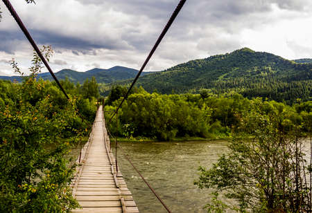 a wooden suspension pedestrian footbridge under fast river in Ukrainian Carpathian, national park...