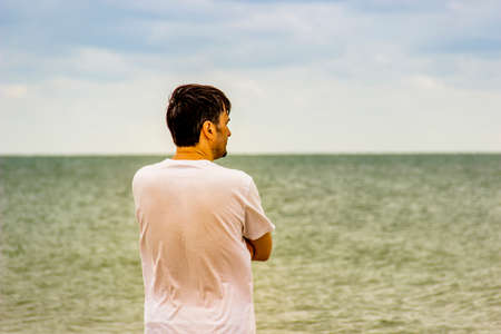 a man in white t-short stay on the seashore and looks into the distanceの写真素材