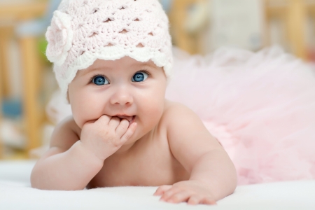 Charming child. Little girl with hat lying on her stomach and sucks fingersの写真素材