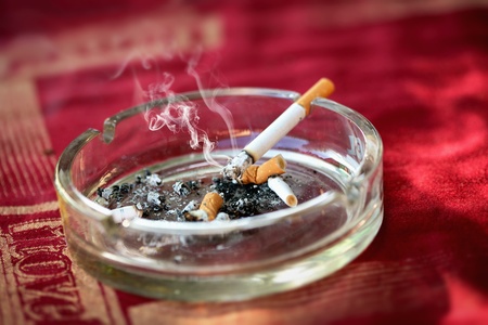 Ashtray with burning cigarette and cigarette buttsの写真素材