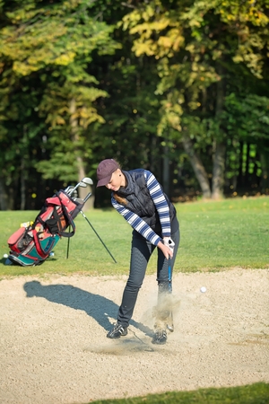 Female golf player put golf ball in sandの写真素材