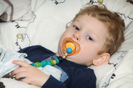 2-year-old boy with pacifier before falling asleep in bedの写真素材