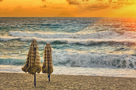 golden sunset on the sea shore and two sunshadesの写真素材