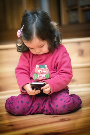 Little cute curious baby girl with dark curly hair holding mobile phoneの写真素材