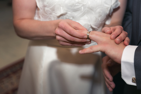 Hands of the groom and bride is wearing a ring on the finger on the day of the wedding ceremony. Gold, symbol, religion, love.の写真素材