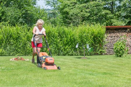 Woman mows the grass in the garden with an electric lawnmowerの写真素材