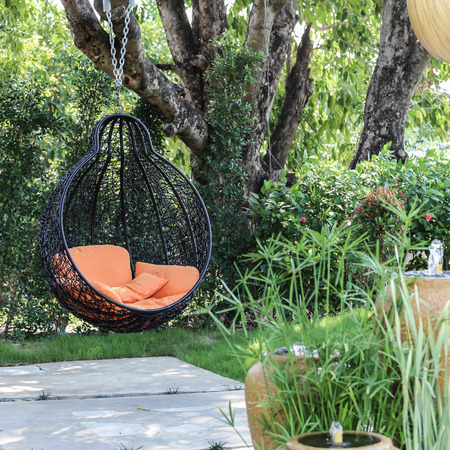Orange pillow on modern swing in the garden.