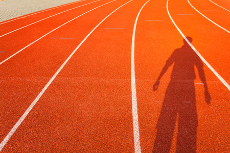 Shadow of man who show extend the arms on red running trackの写真素材