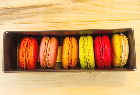 Colorful macarons in black box  on wooden background. Macaron or Macaroon is sweet meringue-based confectionの写真素材