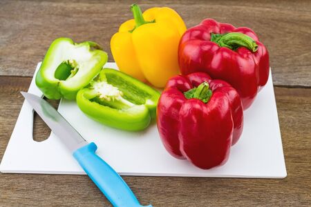 still - life concept colorful sweet bell pepper capsicum  and blue knife in white block   on wooden...