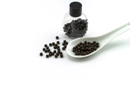 Black pills of traditional medicine or Black bolus near bottle  and white ceramic spoon on white background.の写真素材