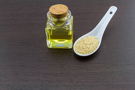 Bottle of sesame oil and sesame seeds in white ceramic spoon  on black wooden backgroundの写真素材
