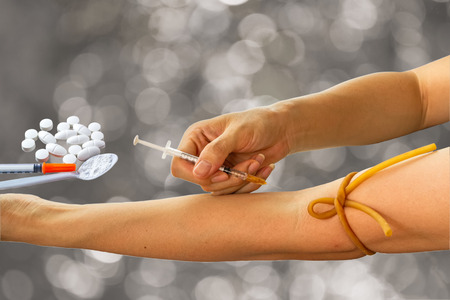 drug injecting by syringe in human arm and drug, syringe insulin and white powder which is similar to heroin on spoon on black bokeh background.の写真素材