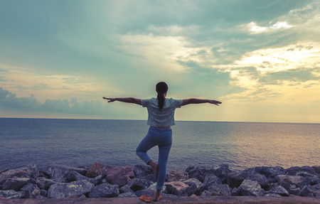 A woman practices yoga on a background of sea and sky with silhouette background,dark tone.