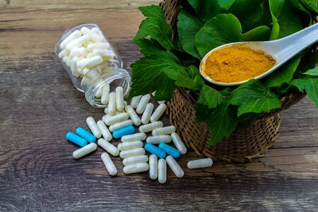 Colorful pill and yellow turmeric powder and green leaf of   White mugwort plant (Artemisia lactiflora) with Green Asiatic Pennywort (Centella asiatica ) on grunge wooden background.の写真素材