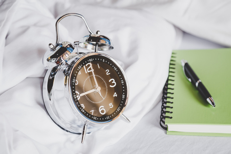 Alarm clock with a pen and notebook on bed in the bedroom at nine o'clock.の写真素材