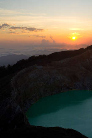 The morning sun rises above a sea of clouds at Kelimutu National Park, revealing a green volcanic lake.の写真素材