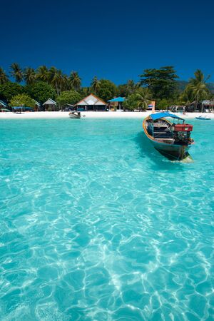 A traditional longtail boat floats in perfect crystal clear water on the island paradise of Ko Lipe, Thailandの写真素材