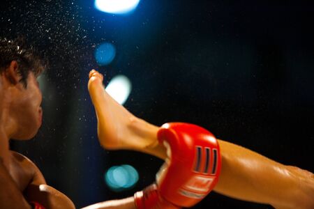 BANGKOK - OCTOBER 12: A kick catches the head of a muay thai boxer and sends sweat flying through the air at Fight Night October 12, 2010 at Bangkok, Thailandのeditorial素材