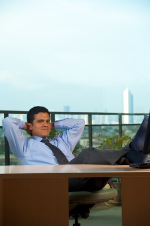 A successful hispanic businessman in his office reclining chair, hands behind his head, looking at camera.  30s latino American male of mixed Brazilian - Mexican descent.の写真素材