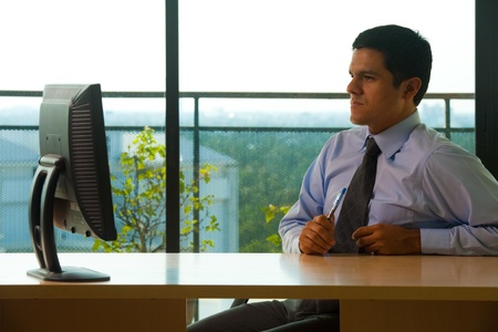 A successful hispanic business executive sitting at office desk looking at his computer monitor.  30s latino American male of mixed Brazilian - Mexican descent.の写真素材