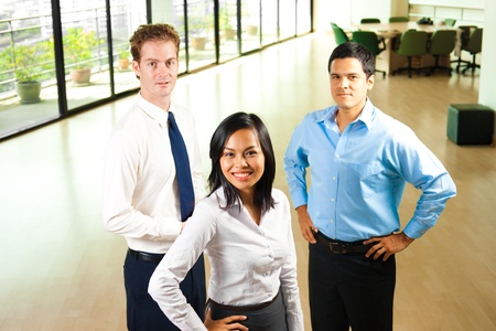 A team of three diverse professional colleagues, a caucasian, asian, and hispanic stand united in a beautiful office environment.の写真素材