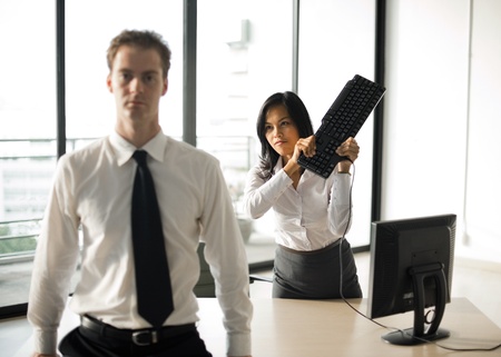 A female office employee swings a keyboard to mock hit her male boss over the head. A female office employee swings a keyboard to mock hit her male boss over the head.