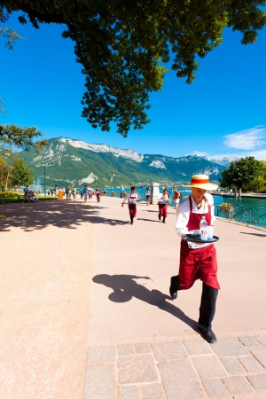ANNECY, FRANCE - AUGUST 25, 2010: An apron wearing waiter runs with a loaded tray around Annecy Lake at the French Alps during the Waiter's Race on August 25, 2010 in Annecy, France. Verticalのeditorial素材