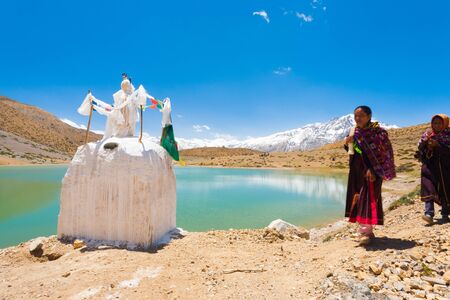 DHANKAR, INDIA - JUNE 7, 2009: Unidentified Buddhist pilgrims walk on pilgrimage past a stupa around a pristine alpine lake in the Himalayas in the Spiti Valley on June 7, 2009 in Dhankar, Indiaのeditorial素材
