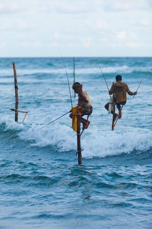 UNAWATUNA, SRI LANKA - MAY 22, 2008: An unidentified Sri Lankan stilt fishermen dips his lure into the waves to catch fish in a uniquely traditional way on May 22, 2008 in Unawatuna, Sri Lankaのeditorial素材