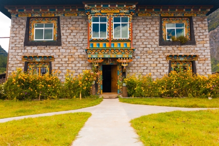 The beautifully decorated front of a traditional Tibetan stone brick house surrounded by a lawn and fresh flowers in Bomi, Tibet, Chinaのeditorial素材
