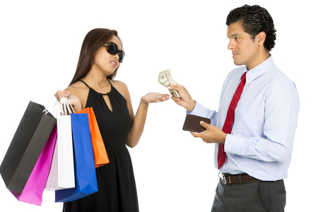 A latino husband gives more cash to his demanding superficial Asian wife holding shopping bags and wearing stylish clothes holding her hand out. Hの写真素材