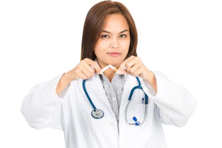 A beautiful female Asian doctor in white lab coat, head angled, looking at camera holds a broken cigarette promoting quitting smoking. Horizontalの写真素材