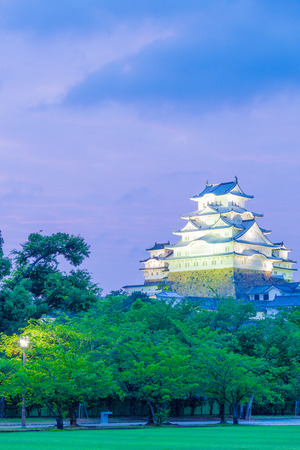 Himeji-jo castle lighted at evening sunset with deep purple sky and foreground trees from nearby park in Himeji, Japan after 2015 completely renovated. Vertical copy spaceのeditorial素材