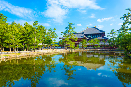 Pedestrian path and tranquil lake reflecting the front red entrance gate to Daibutsuden seen in distance on beautiful, sunny blue sky morning at Todai-ji temple in Nara, Japan. Horizontal copy spaceのeditorial素材