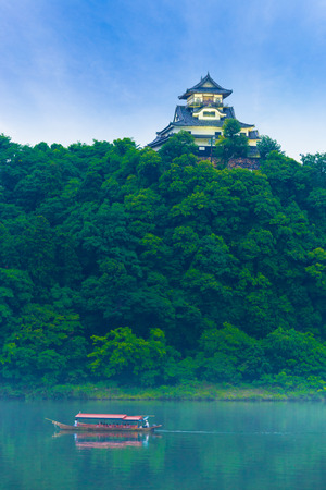 A tourist cruise boat on the Kiso River below Inuyama Castle stronghold atop a forest hill on a blue sky day in Gifu Prefecture, Japanのeditorial素材