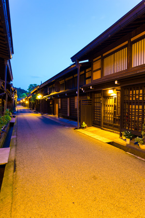 Takayama, Japan - July 10, 2015: Traditional Japanese dark wooden homes, restaurants lighted at night line empty pedestrian street in Kamisannomachi district of historic old town at dusk. Verticalのeditorial素材