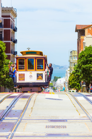 San Francisco, USA - May 19, 2016: Oncoming cable car is full of outside hanging and platform standing tourists with bay water background in sunny Powell Street in California. Verticalのeditorial素材