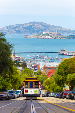 San Francisco, USA - May 19, 2016: Approaching cable car full of tourists coming uphill with Angel and Alcatraz Island, bay water in background on Hyde Street in sunny Californiaのeditorial素材